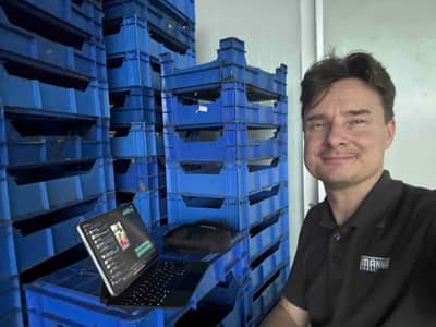 Ykä Marjanen with a laptop beside stacked production crates in a facility.