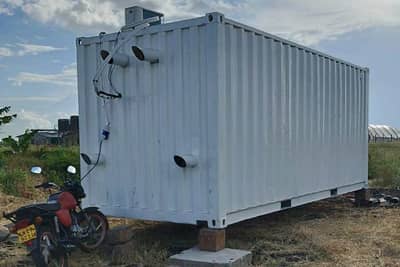 A container-based production setup in a field, with ventilation connections on its outer wall.